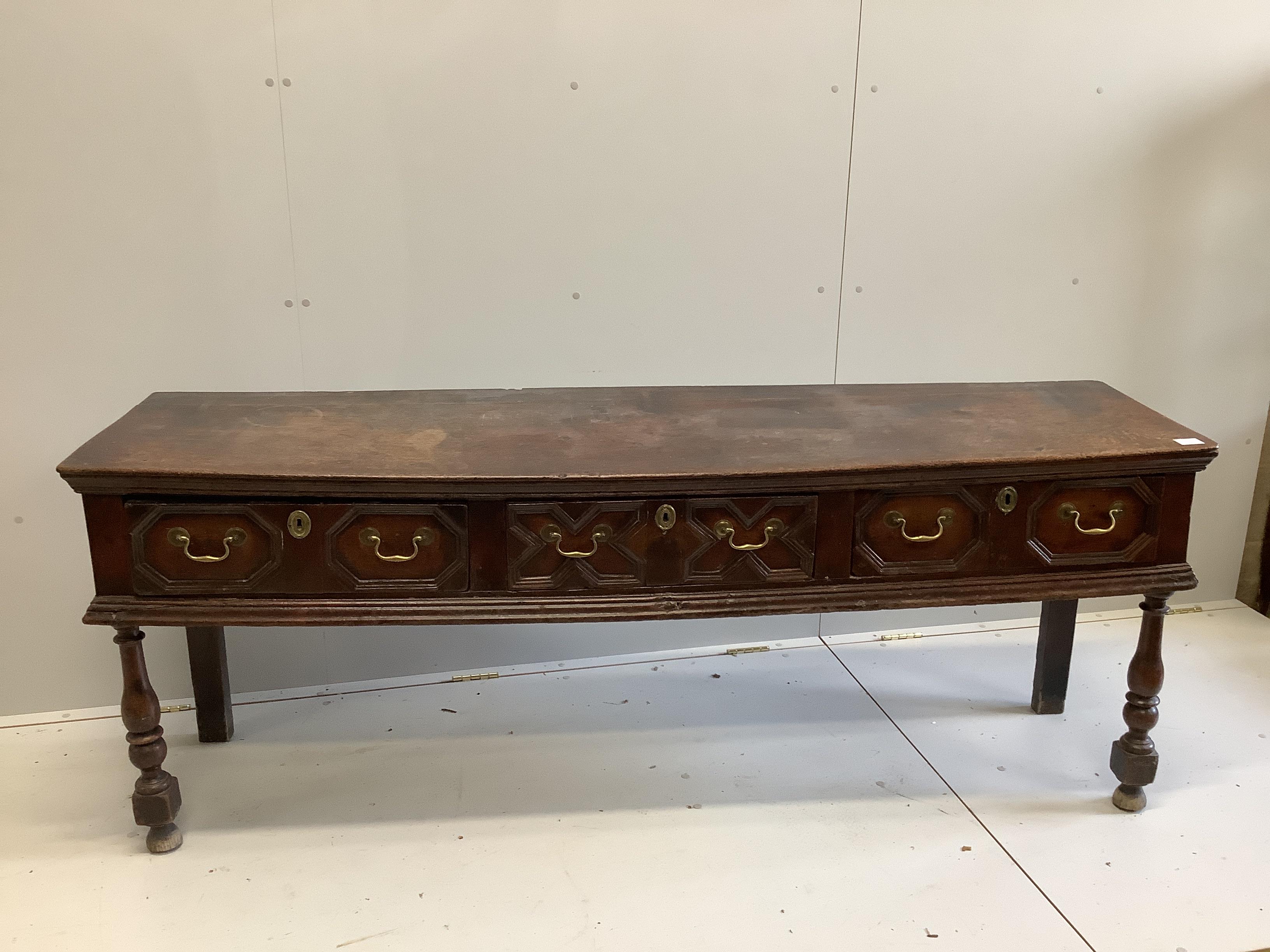 An 18th century oak low dresser fitted with geometric moulded drawers and brass handled over turned supports, length 193cm, width 49cm, height 74cm
